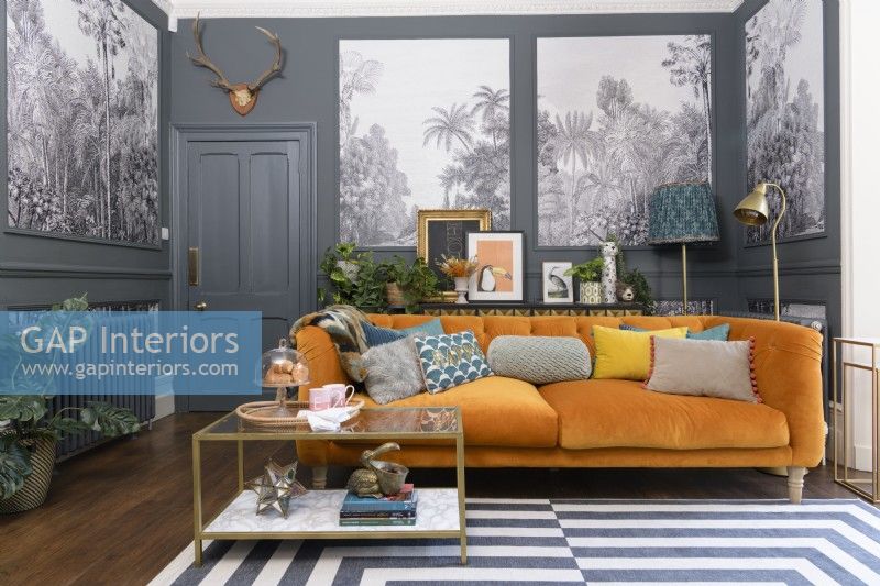 Orange velvet sofa in a grey living room with panels infilled with monochrome tropical tree patterned wallpaper
