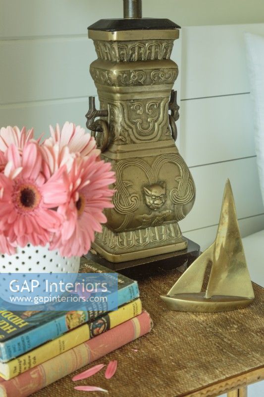 An urn-shaped metal lamp and a tiny brass sailboat grace a bedside table.