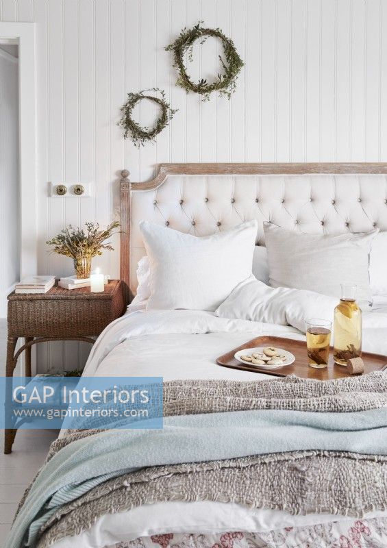 Country bedroom with rustic wreaths on white wall above bed