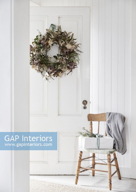 Christmas present on wooden chair and rustic wreath on white door