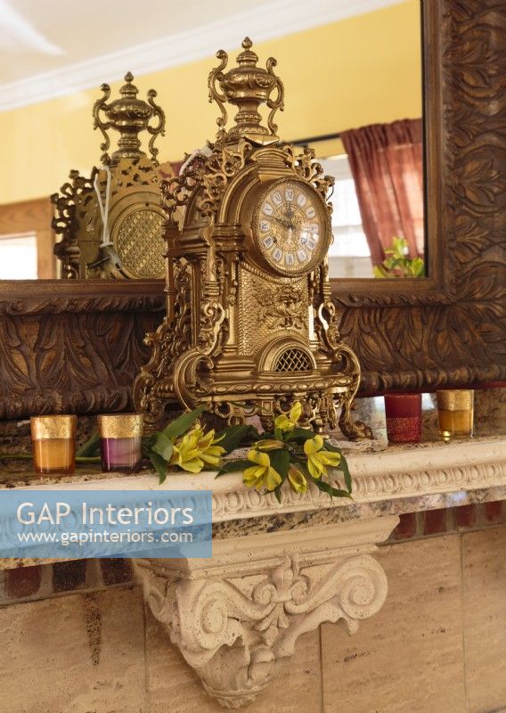 Flanked by jeweled-color votives, a one-of-a kind antique Italian brass clock presides over the carved stone mantel.
