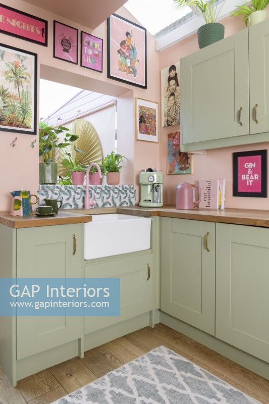 White butlers sink in the corner of a colourful pale pink and green Shaker retro style kitchen with an open hatch through to a conservatory