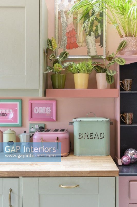 Detail of retro kitchen wooden counter top with a pale green vintage bread bin and retro style pink toaster