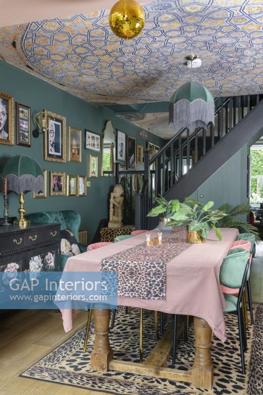Open plan dark green dining area with mosaic wallpapered ceiling and tassle fringed art deco style lamps