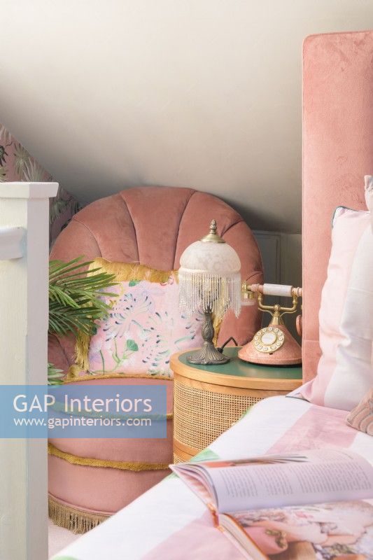 Pink vintage chair and bedside table with fringed table lamp and retro style pink telephone