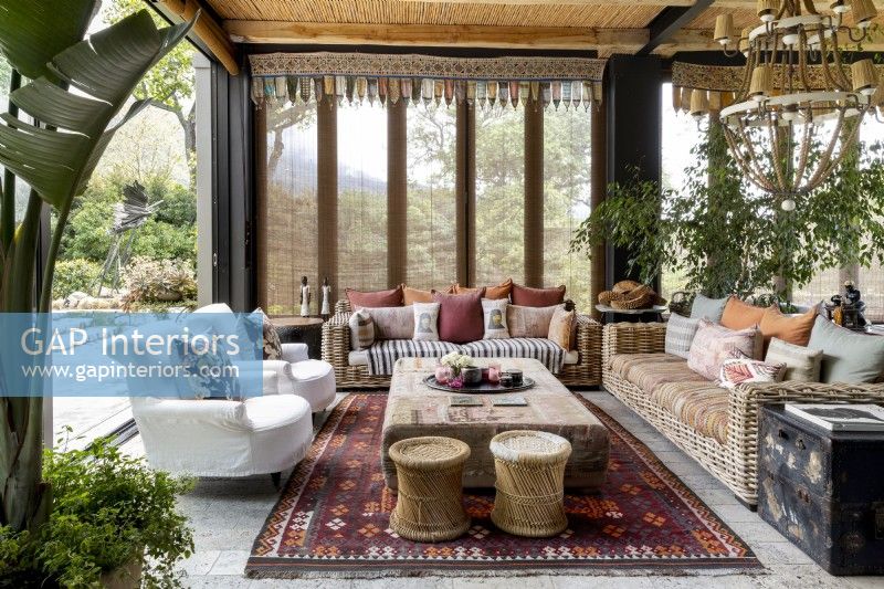 Enclosed veranda with rattan furniture, slip covered armchairs and plants  