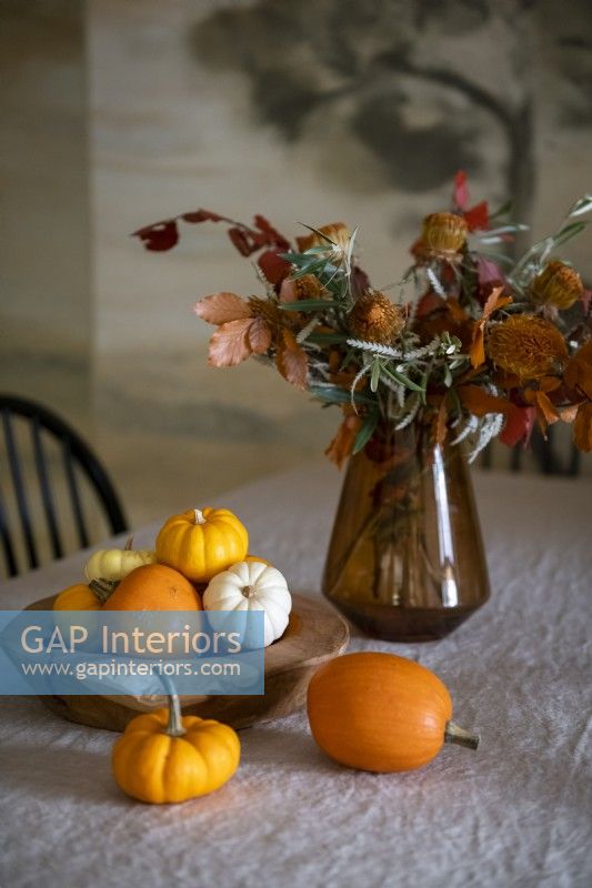 Autumnal display of small pumpkins and flowers in vase on table