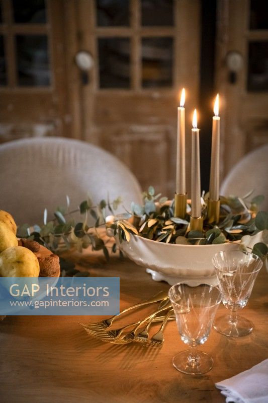 Candles lit in bowl of decorative foliage on dining table
