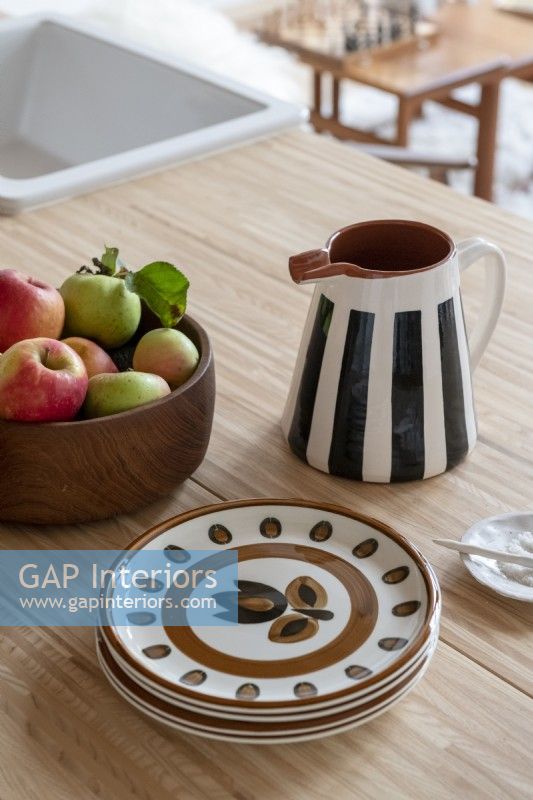 Fruit bowl, plates and striped ceramic jug on wooden table