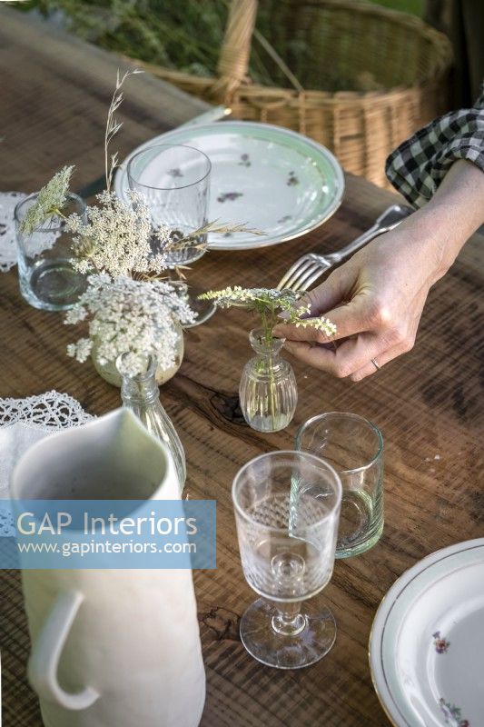 Woman putting wildflowers into a glass vase on outdoor dining table