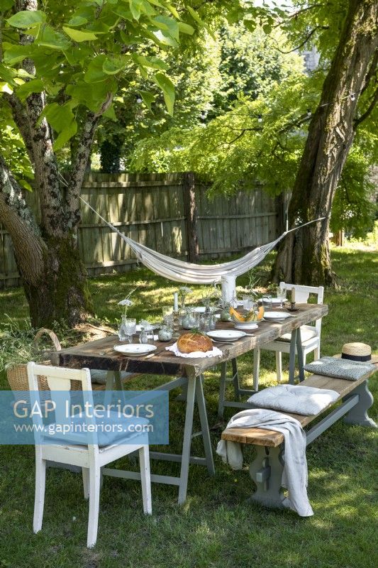 Rustic outdoor dining area on grass in shade of trees in summer