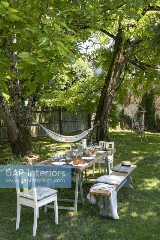 Country garden with dining table laid for lunch under shade of trees 