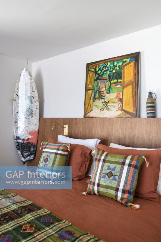 Surfboard and artwork in modern bedroom with patterned bedding