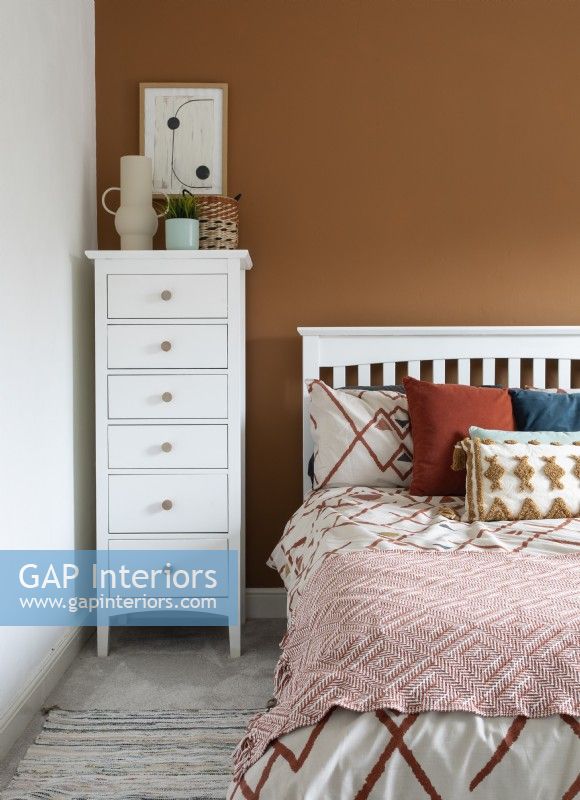 Tall white chest of drawers against brown painted wall in bedroom