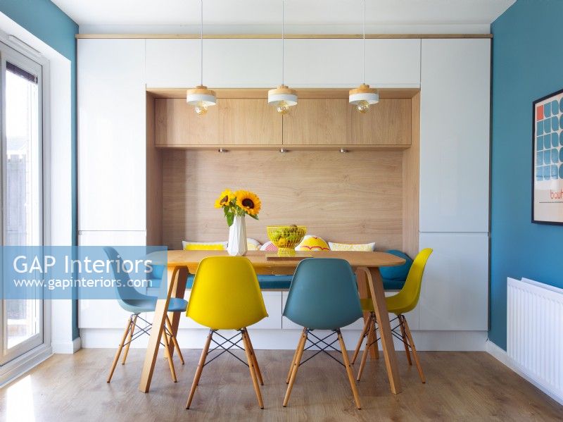 Blue and yellow chairs around wooden dining table with alcove seat
