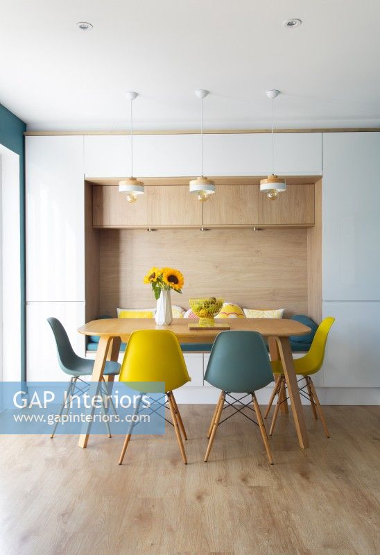 Blue and yellow chairs around dining table with built-in bench seat