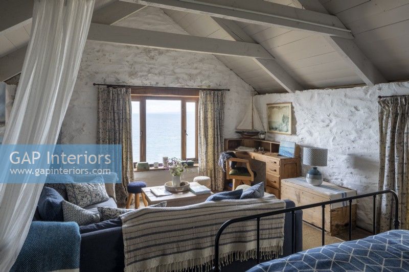 Comfortable bedroom with sitting area, whitewashed walls, and beams, view of the sea from the window.
