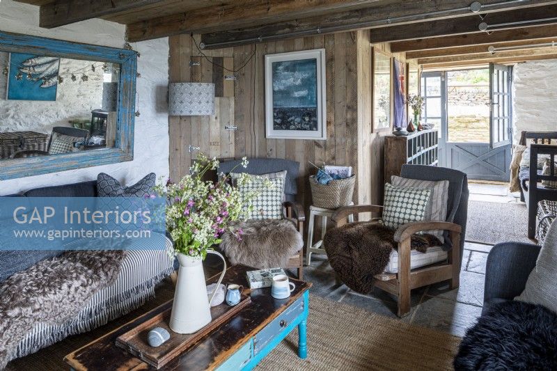 Living room with rustic clad walls, wooden beams and comfortable furniture.  Large vase of wild flowers picked from the surrounding countryside.