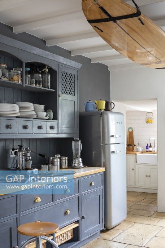 Sally and John Biddle's house in Cornwall, Blue painted kitchen cupboards, and modern Smeg fridge, with surfboard attached to ceiling beams