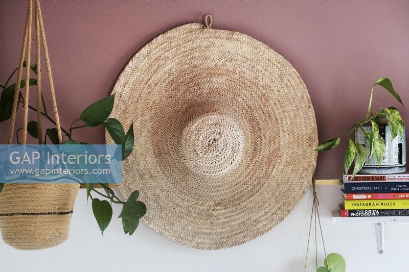 Detail of large straw hat on wall with houseplants on shelf