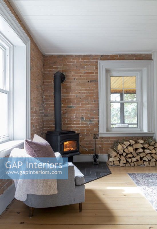 Armchair next to lit woodburning stove against exposed brickwork wall