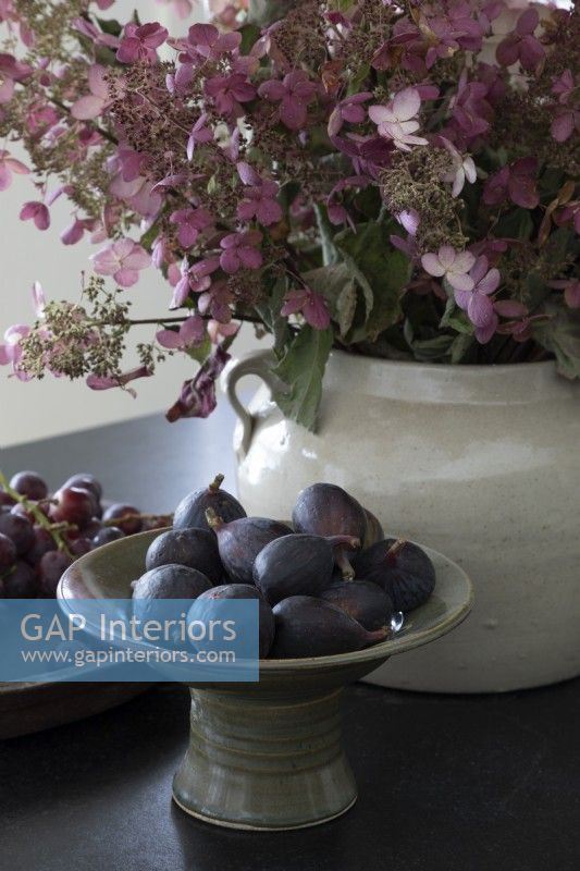Bowl of fresh figs next to flower arrangement in ceramic pot 