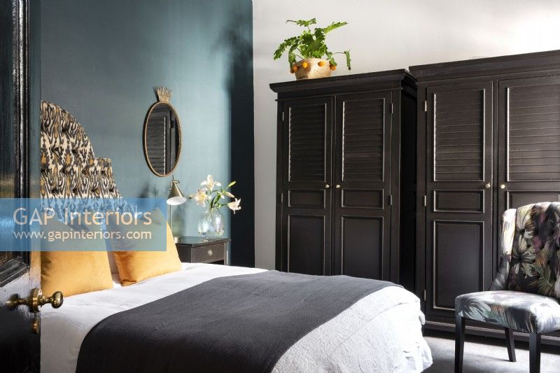 Bedroom with upholstered bed headboard,duck blue feature wall and black cupboards