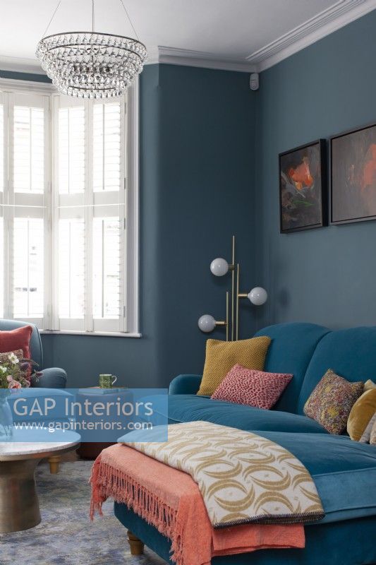 Bold sitting room corner with dark blue walls and velvet sofa