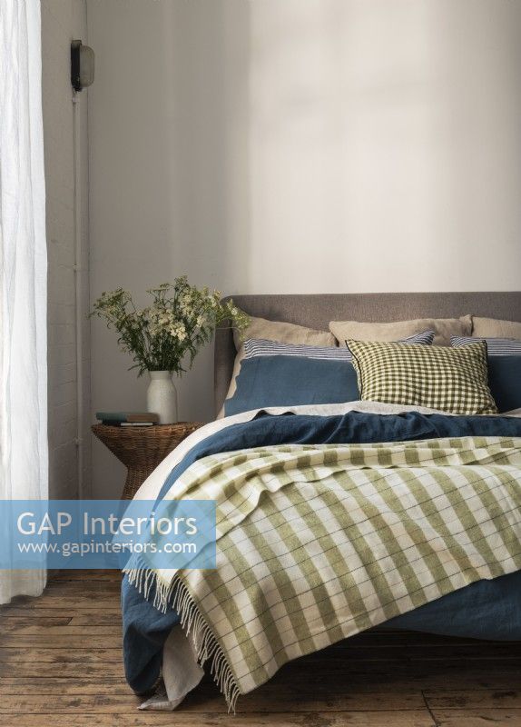 Green checked blanket on double bed with blue bedlinen