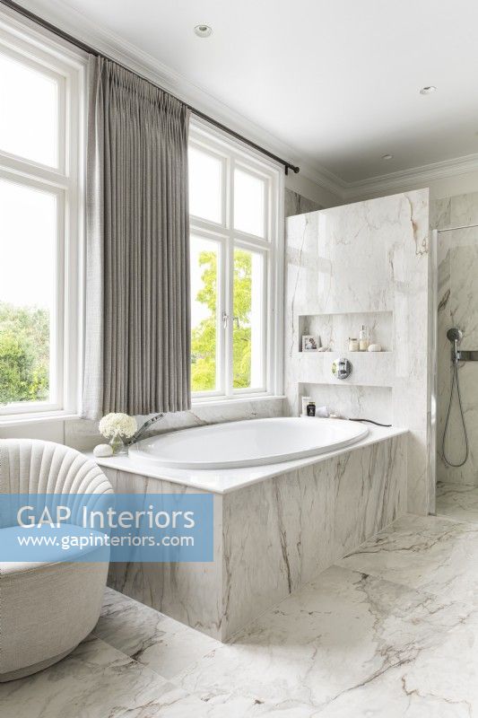 Classic, contemporary marble bathroom with bath by window and shower. 