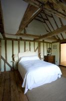 Boonshill Farm, East Sussex. Interior of bedroom with wooden floorboards, exposed beams and bed with french wooden headboard. 