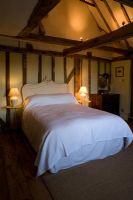 Boonshill Farm, East Sussex. Interior of bedroom exposed beams, french bedhead and old metal side tables. 