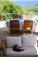 Corfu, Greece. Yialiskari House Villa near Kalami. Terrace with wicker loungers, cat, table and view to Albanian Mountains