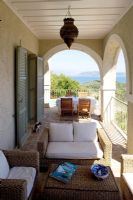 Corfu, Greece. Yialiskari House Villa near Kalami. Terrace with wicker loungers, table and view to Albanian Mountains