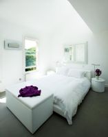 White modern bedroom with bed, blanket box and bedside table with vase of stocks
