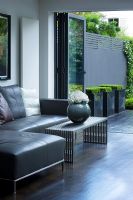 Contemporary living room with grey leather corner sofa, vase and coffee table, leading out to patio and garden designed by Charlotte Rowe