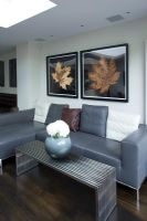 Contemporary living room with grey leather sofa, metal coffee table with modern vase and leaf prints on wall