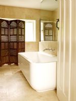 Modern bathroom with bath, large sandstone tiles and wooden screen