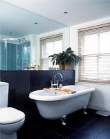Classic bathroom with freestanding roll top bath, large mirror and black slate wall and floor tiles 