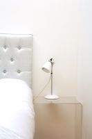 Detail of bed with upholstered headboard and perspex bedside table with lamp