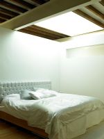 Modern white bedroom with upholstered headboard,soft furnishings and skylight above bed