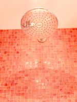Detail of shower head on pink mosaic tiled walls