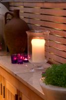 Garden at night with candles on marble shelf, old terracotta urn and wooden trellis
