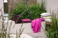 Rendered seating area in garden with raised bed, cushions and bright pink throw