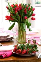 Red tulips in a vase and plate of strawberries on dining table
