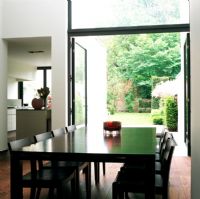 View of dining table with kitchen and open doors to garden in background