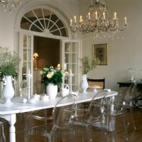 Vase of flowers on dining table with illuminated chandelier and Louis Ghost chairs