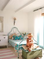 Young girl sitting on pillow next to iron bed 