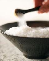 Human hand pouring bath salts with spoon in bowl