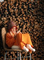 Young girl knitting on a chair in front of a wood pile